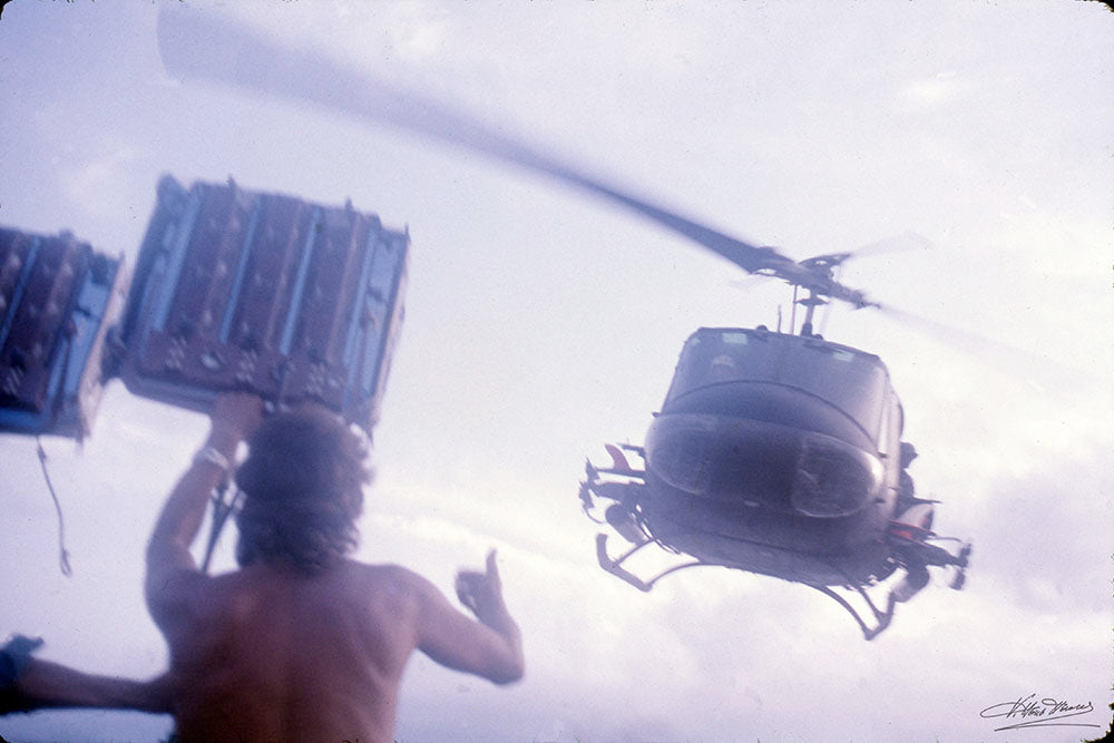 Crew member holding a light rig as a helicopter passes low overhead, signed Apocalypse Now behind-the-scenes photo by Vittorio Storaro